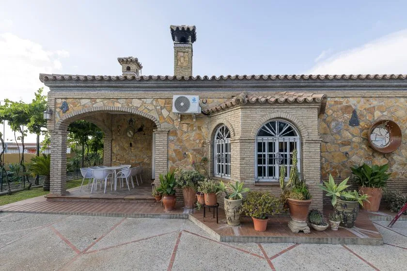 A stone building with arched windows and a shaded patio with outdoor seating.