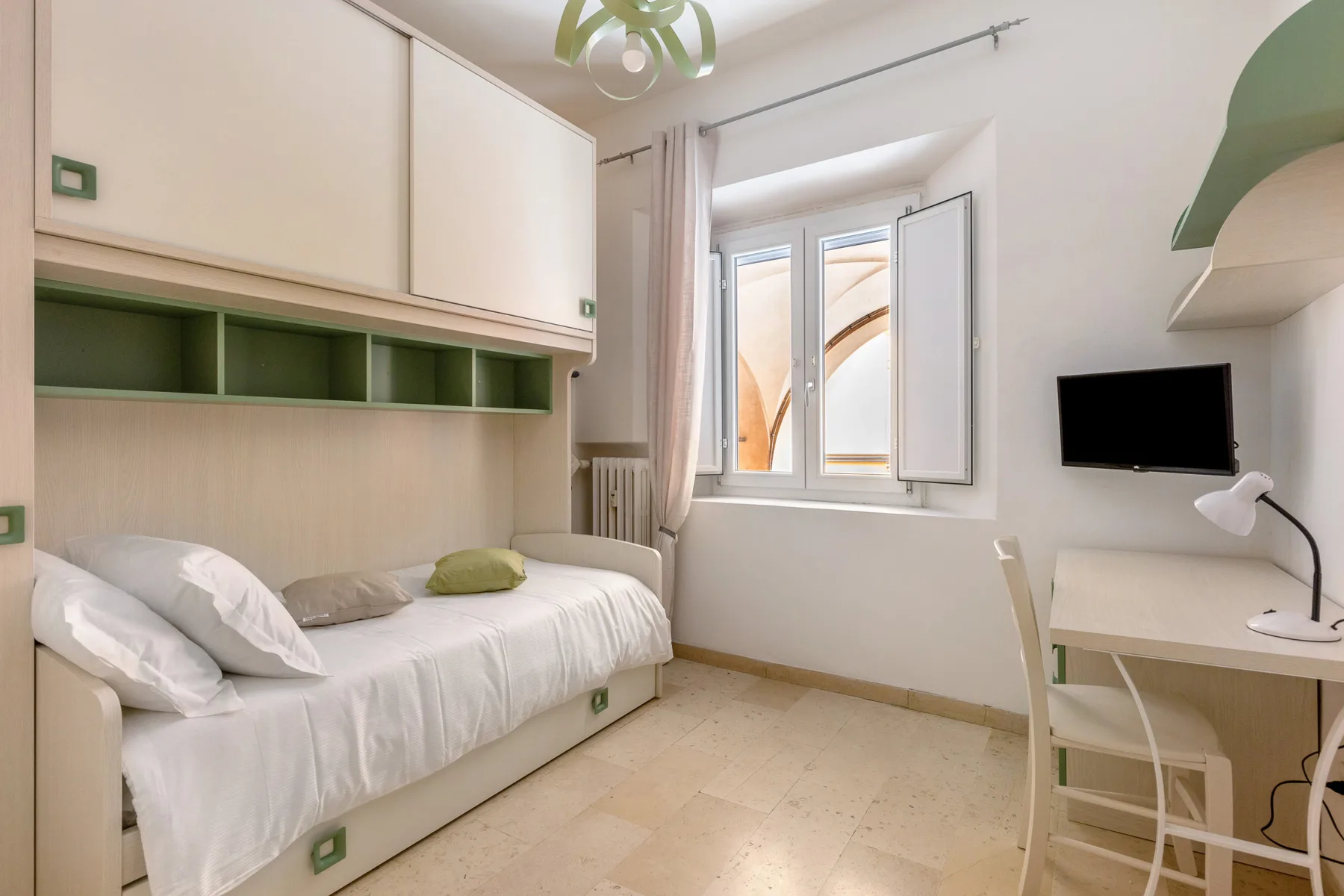 A bedroom with a single bed, a desk, and an open window.