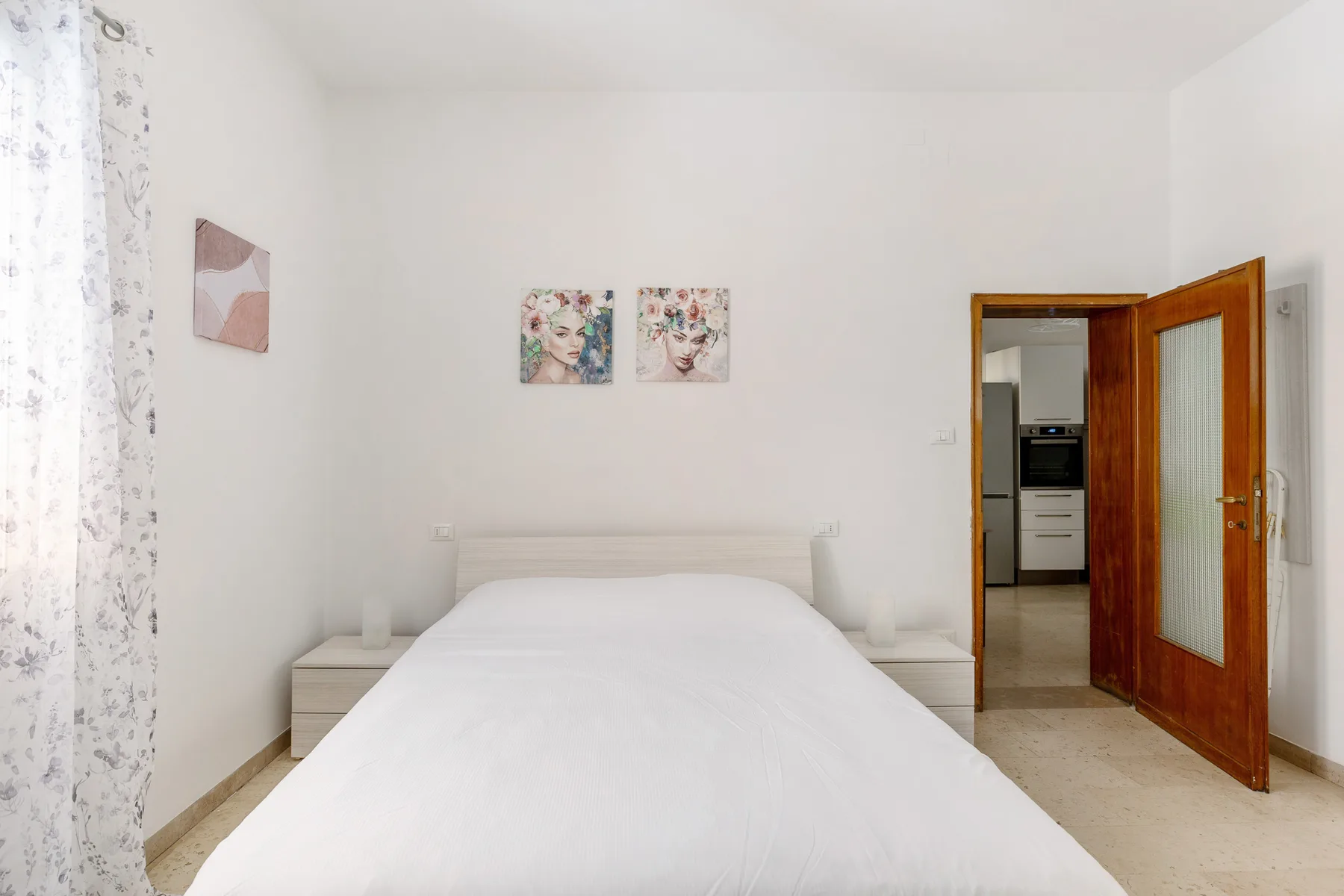 A bright bedroom with a large bed, bedside tables, and an open wooden door.