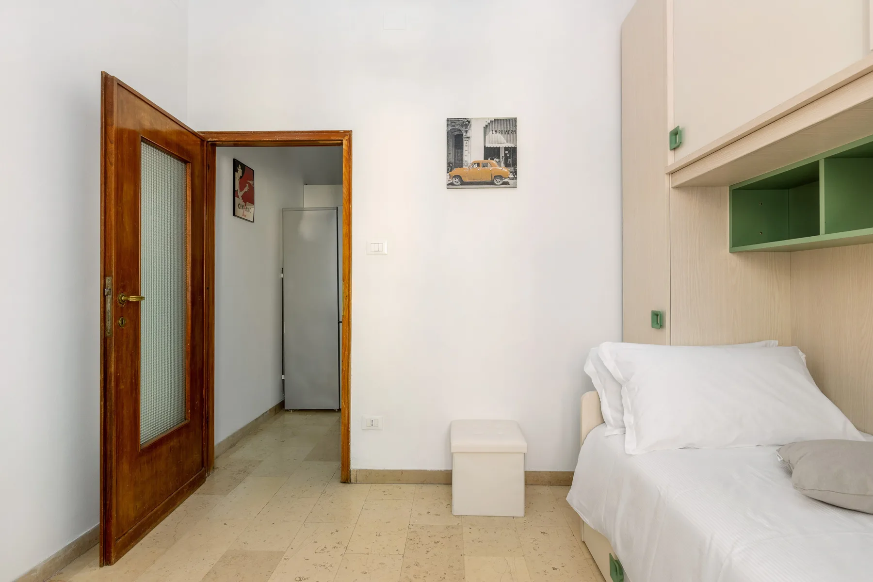 A bedroom with a white bed and an open wooden door leading to a hallway.