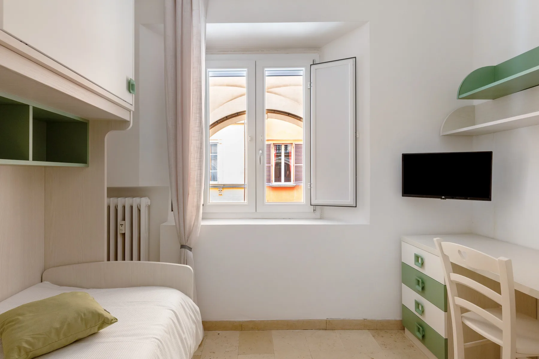 A compact bedroom with a bed, window, and wall-mounted television.