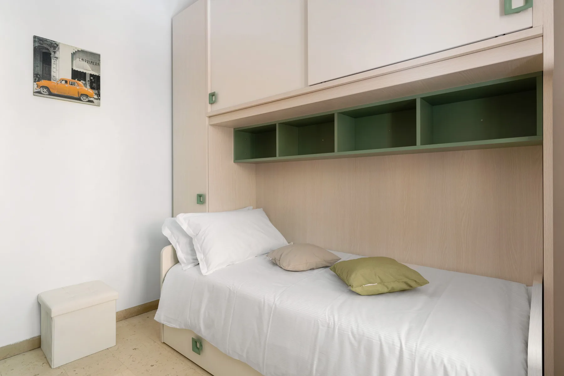 A bedroom with a single bed beneath built-in shelving.