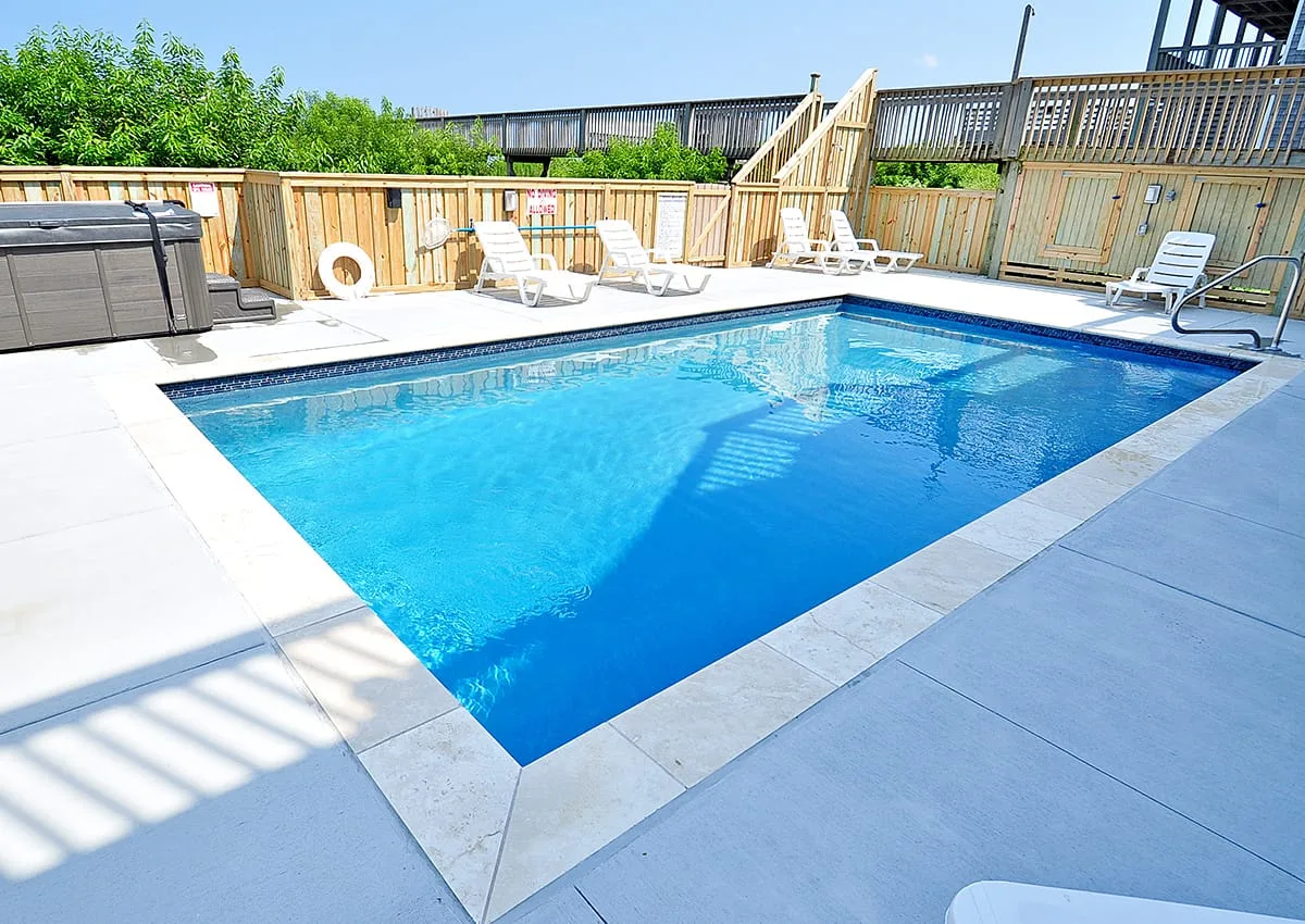 An outdoor swimming pool surrounded by a paved deck and lounge seating.