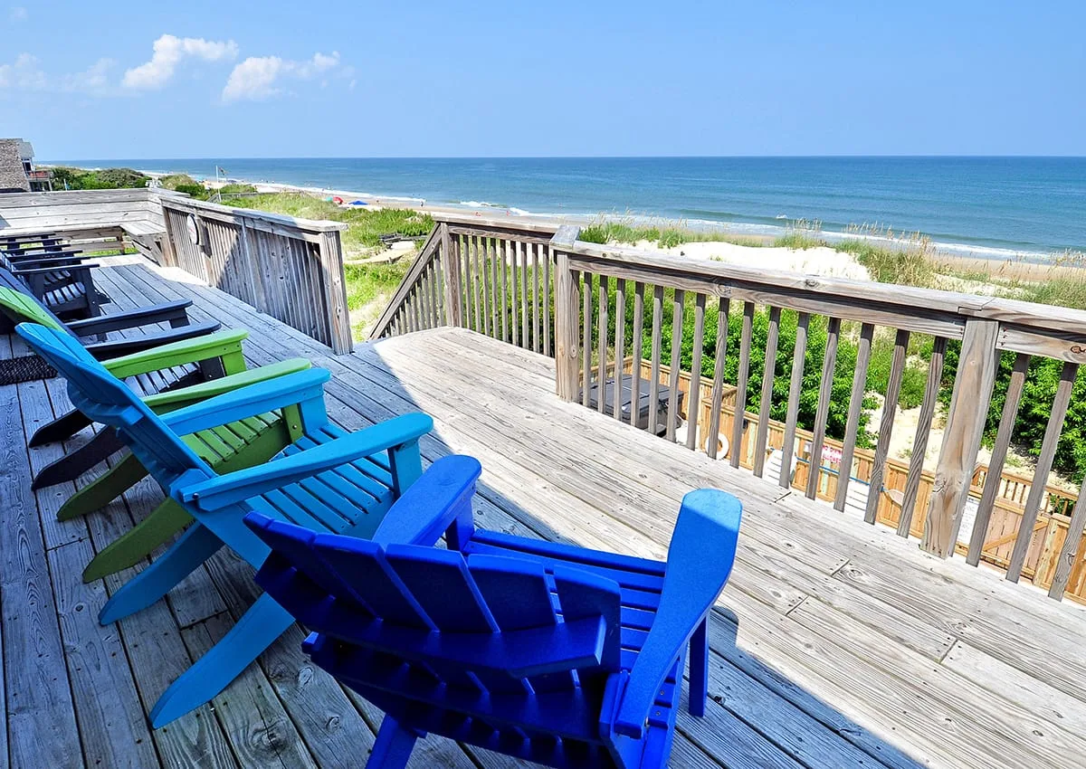 A wooden deck with colorful seating overlooks the beach and ocean.