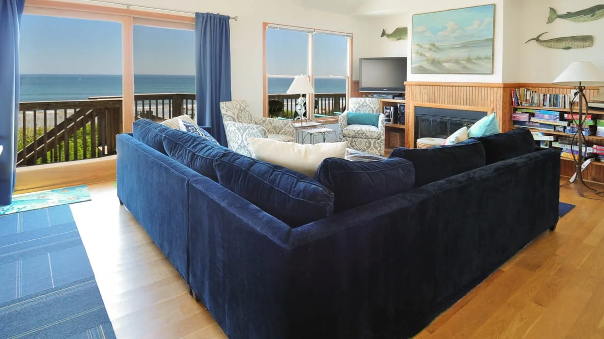 A bright living room with blue seating, large windows, and a view of the ocean.