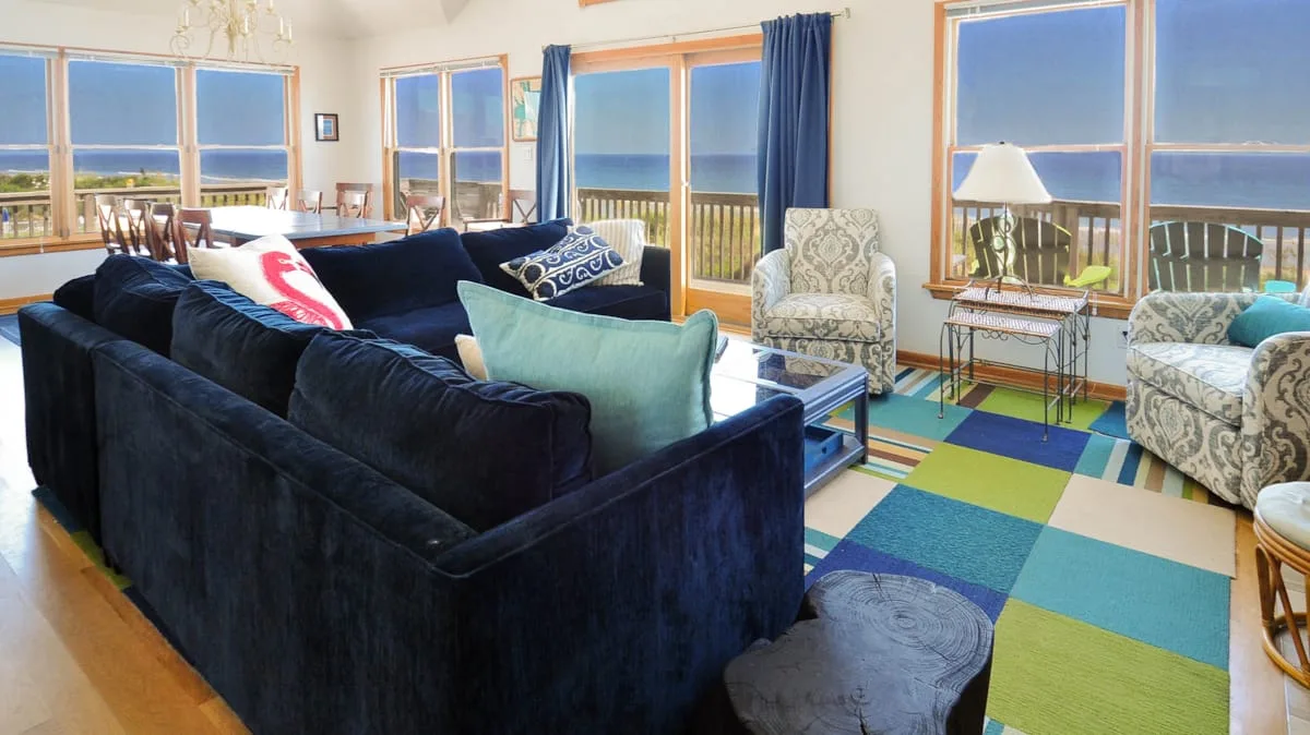 A bright living room with seating arranged beside large windows overlooking the water.