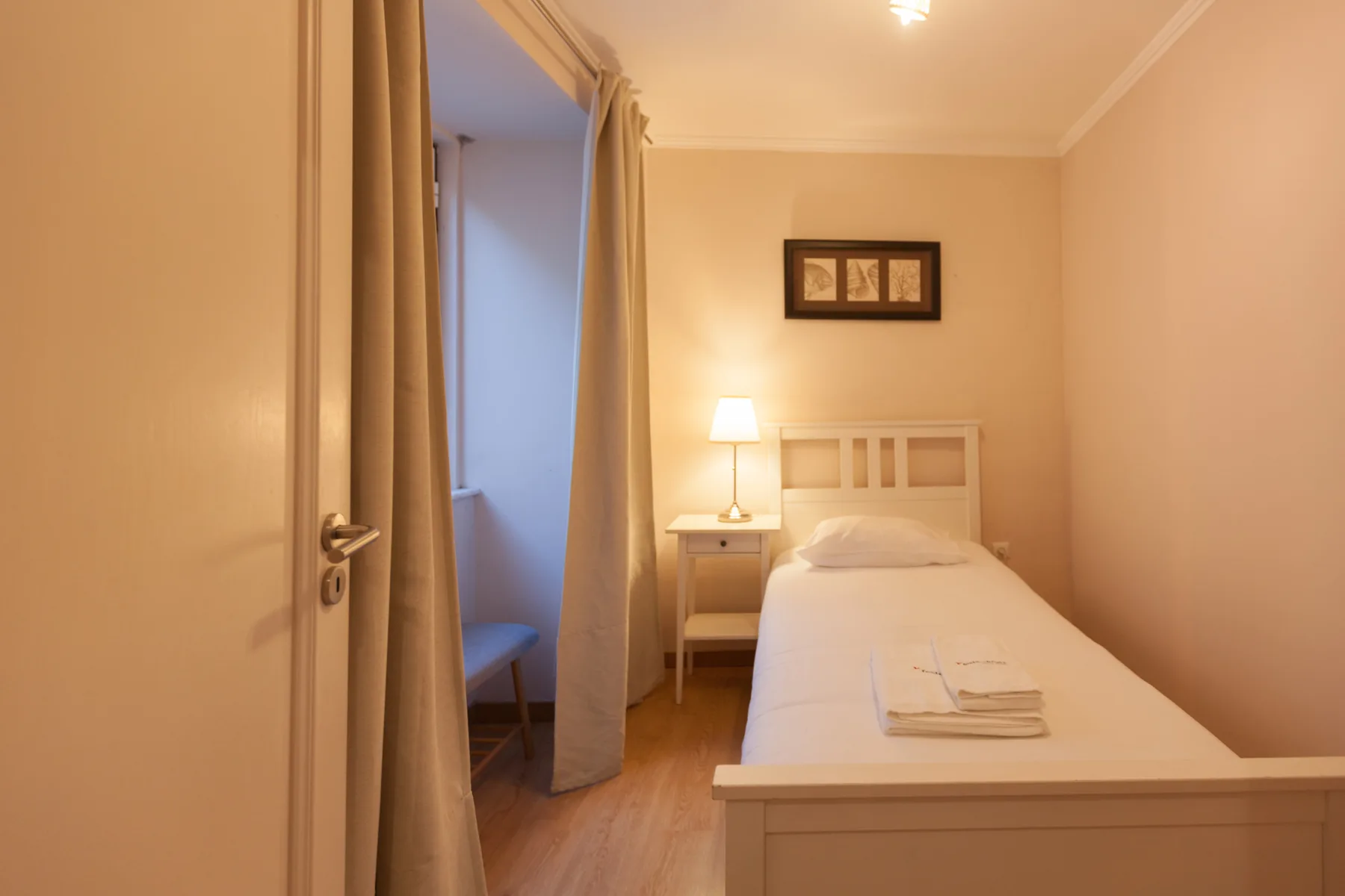 A bedroom with a single bed, bedside table, and a curtained doorway.