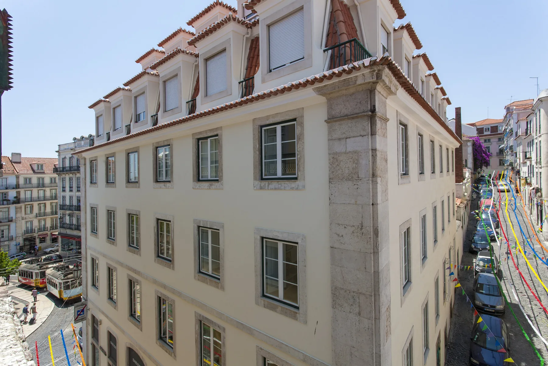 A cream-colored corner building overlooks a narrow street decorated with colorful streamers.