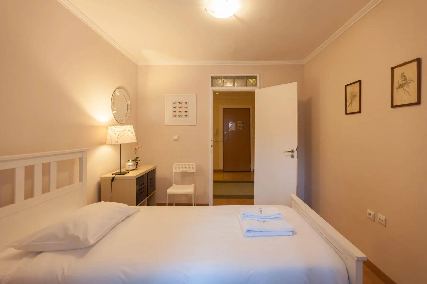 A bedroom with a neatly made bed, bedside lamp, and open doorway.