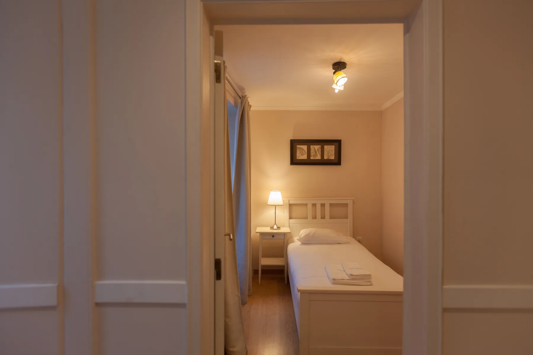 A bedroom with a single bed, bedside table, and framed artwork.