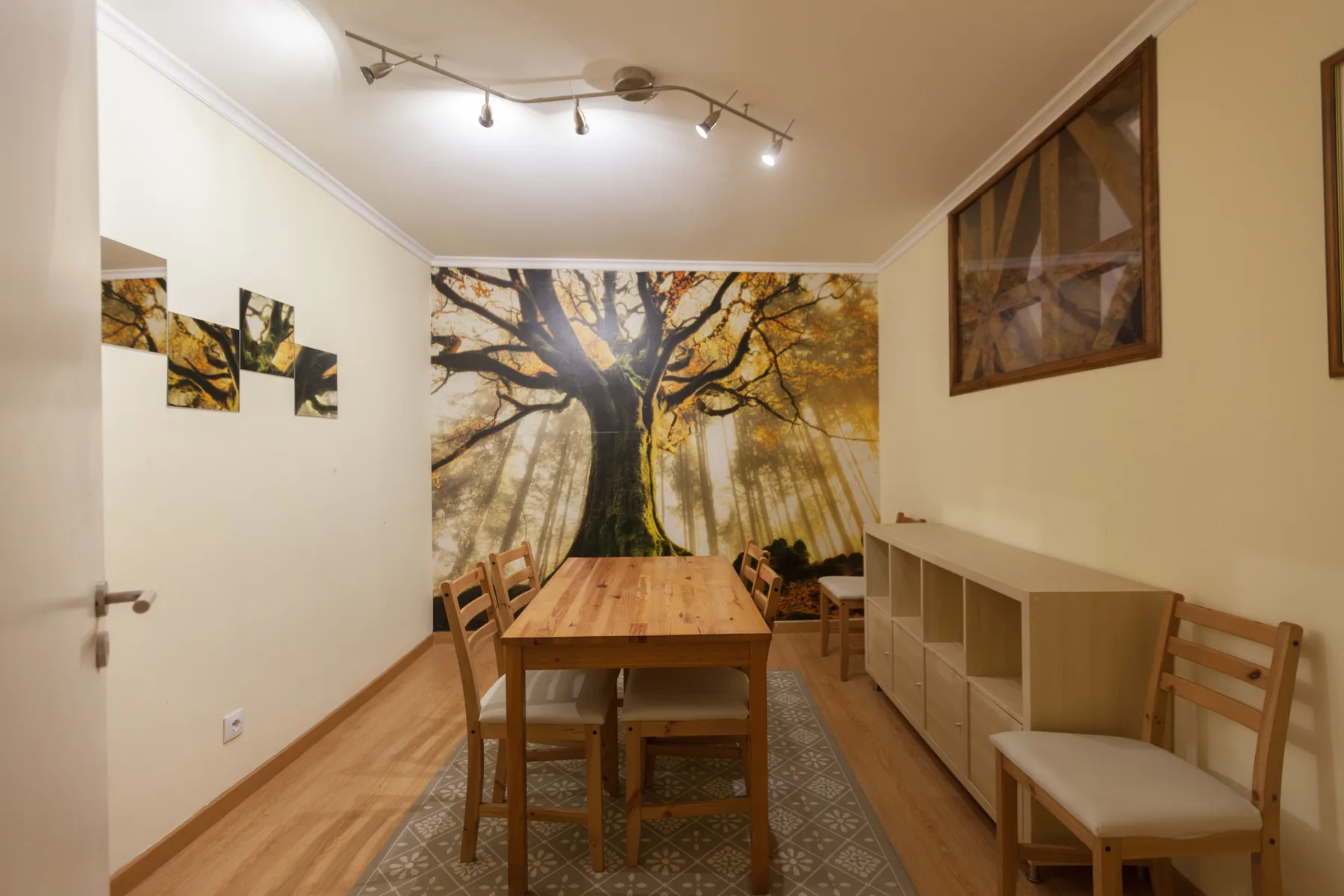 A dining area with a wooden table and chairs beneath a large tree mural.