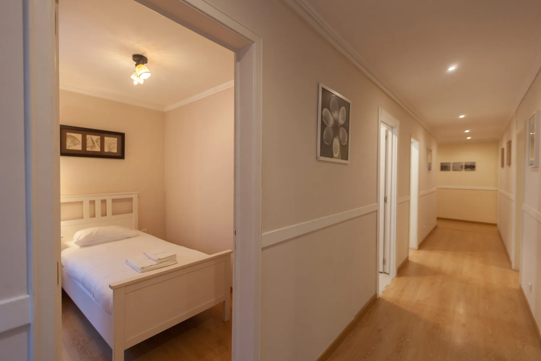 A bedroom with a white bed opens onto a hallway.