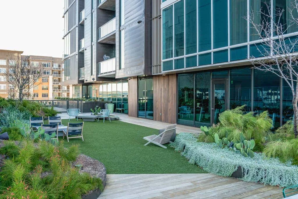Un patio ajardinado con asientos al aire libre junto a un edificio moderno con fachada de vidrio.