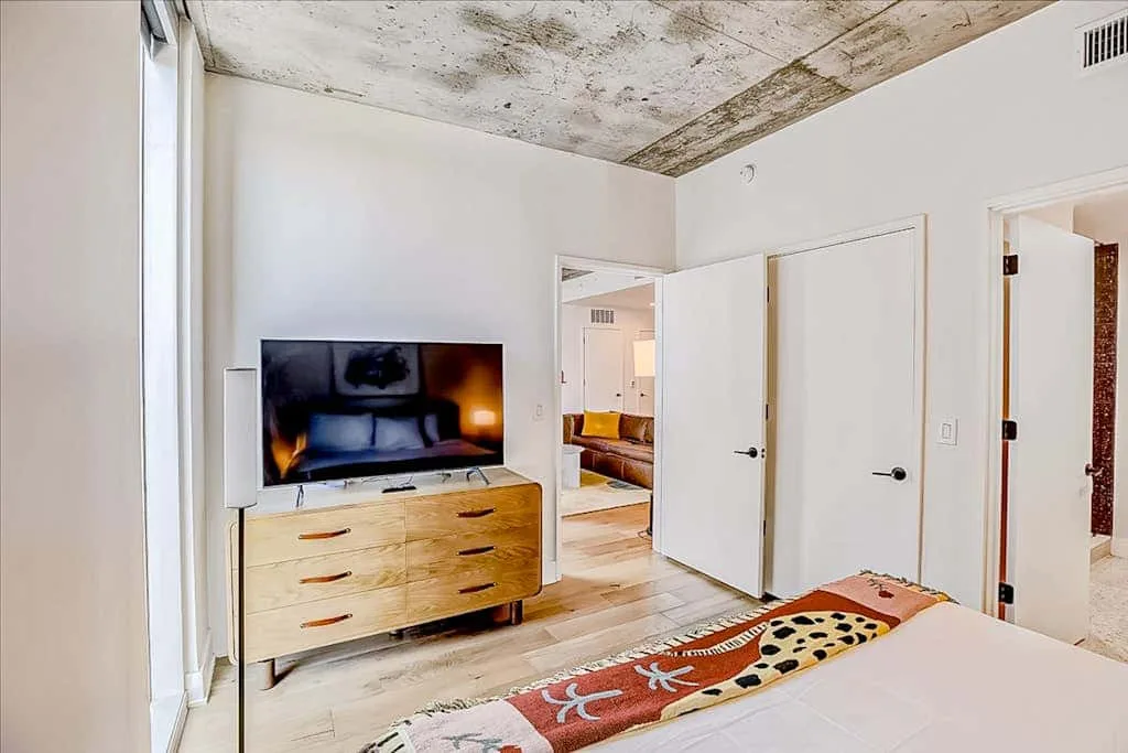 Un dormitorio con un televisor sobre una cómoda de madera y una colcha estampada.