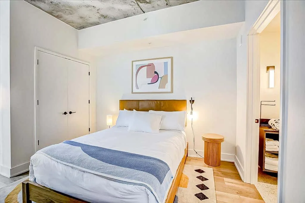 Un dormitorio con una cama tendida y una obra abstracta sobre el cabecero.