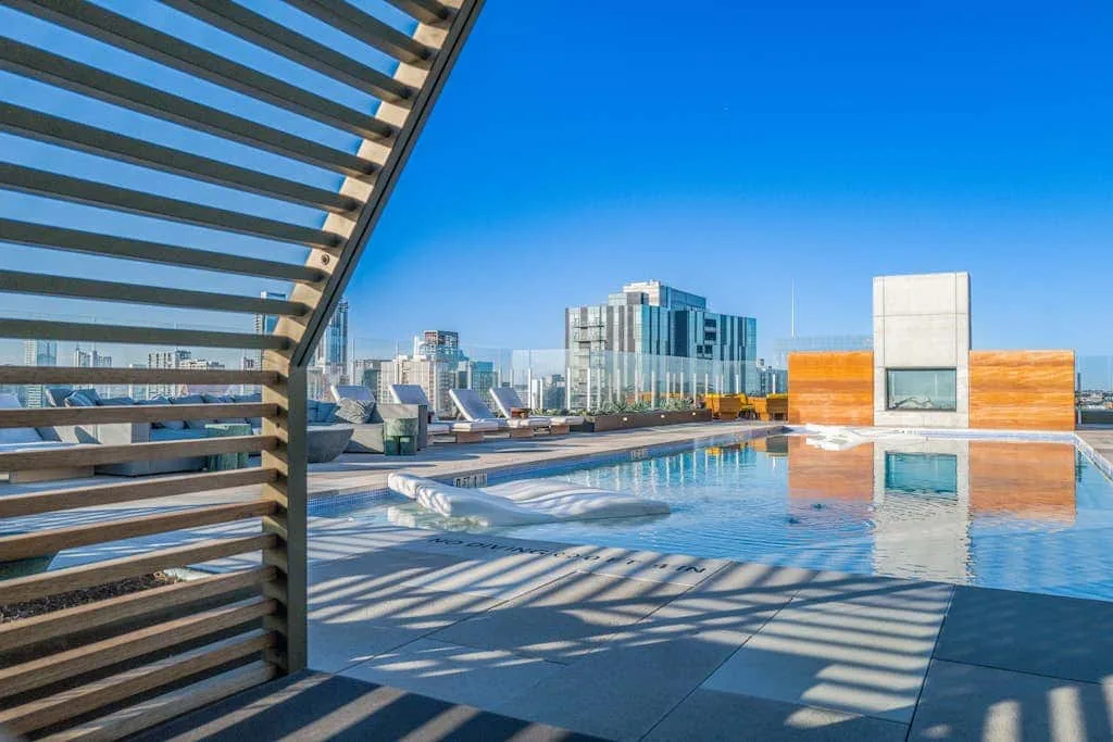 Una piscina en la azotea contempla edificios de la ciudad junto a una pérgola de listones.