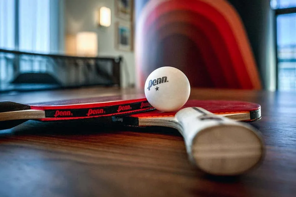Una pala de ping-pong y una pelota descansan sobre una mesa en un área recreativa interior.