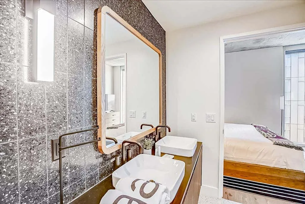 Un lavabo de baño con un espejo grande y una puerta abierta hacia un dormitorio.