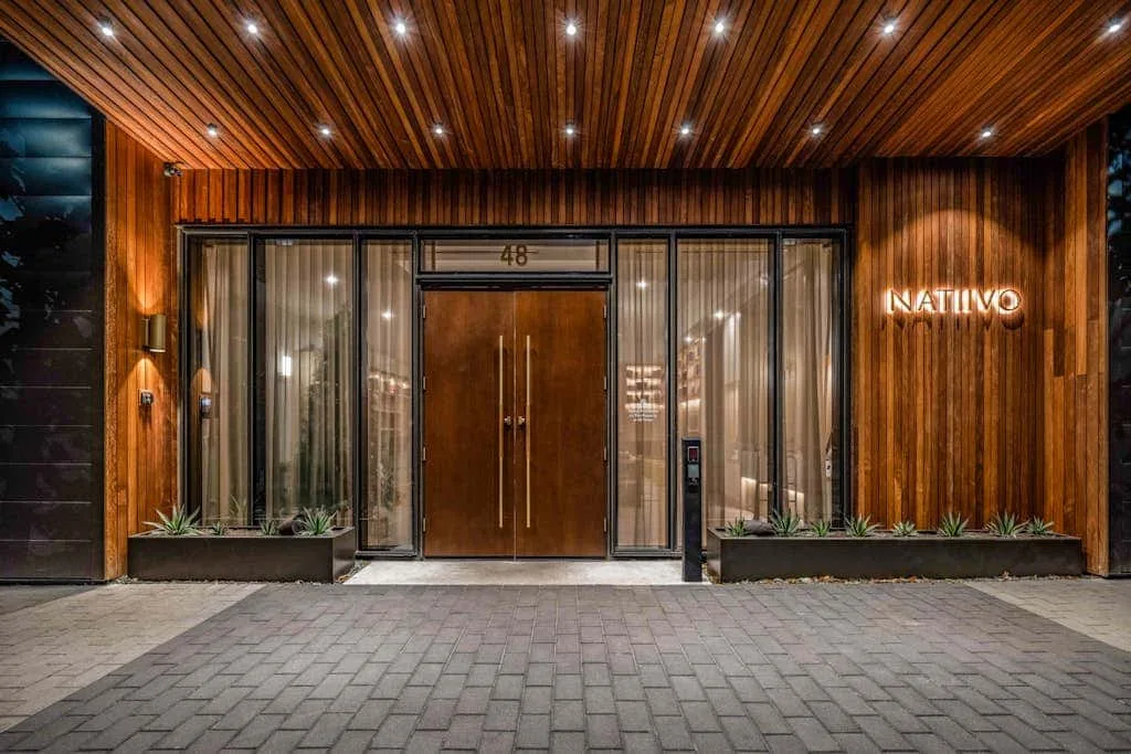 Una entrada de madera con puertas de vidrio y jardineras.