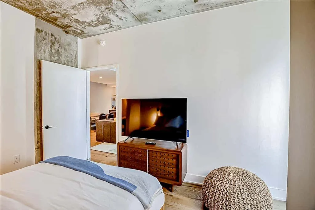 Un dormitorio con una cama, un televisor y un puf tejido.