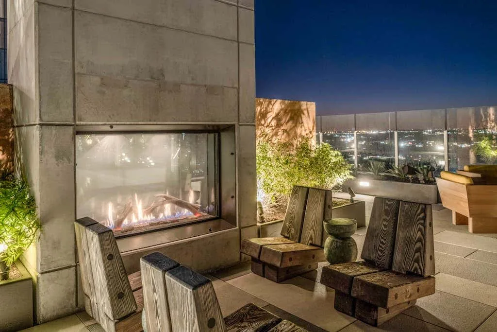 Un patio al aire libre con asientos bajos y una chimenea encendida.