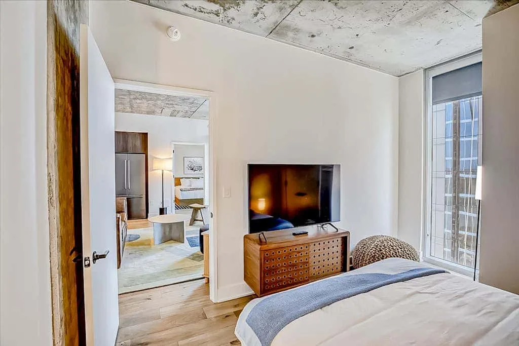 Un dormitorio con una cama, un televisor y una vista a otra habitación a través de la puerta.