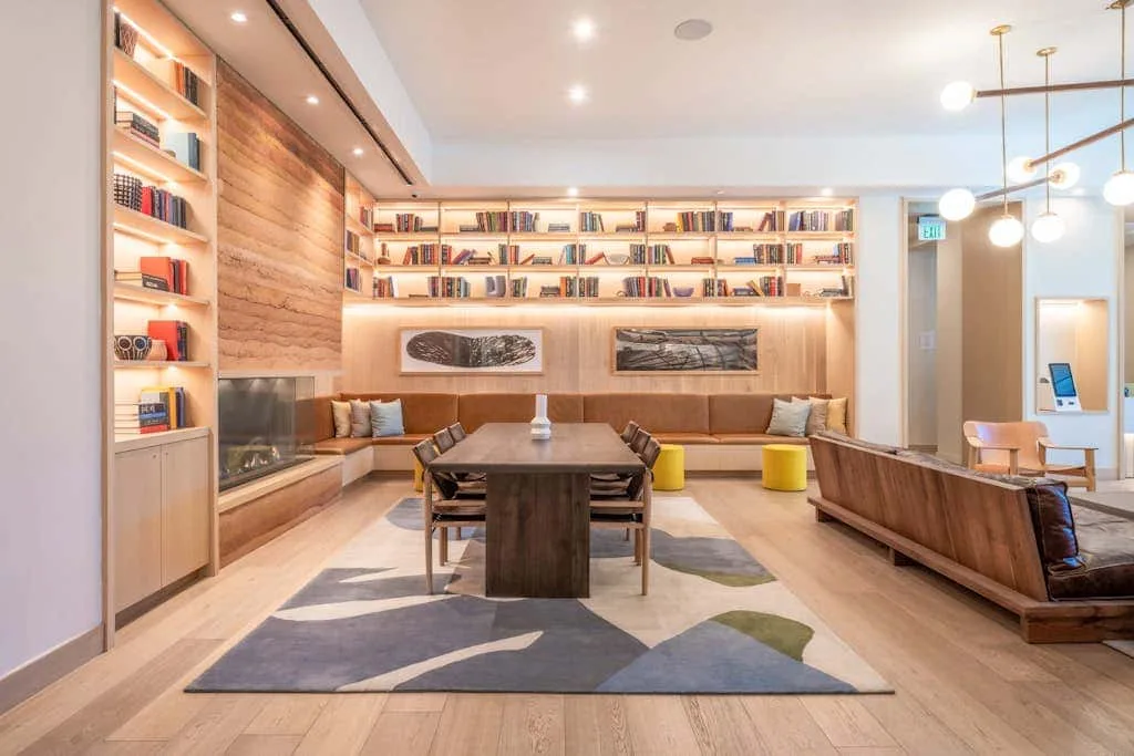 Una sala de estar con una mesa larga, asientos y estanterías iluminadas.