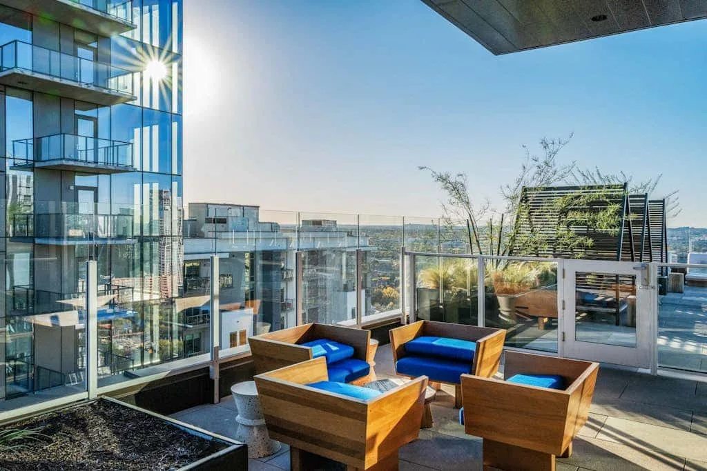 Una terraza en la azotea con asientos al aire libre y barandillas de vidrio da a edificios cercanos.