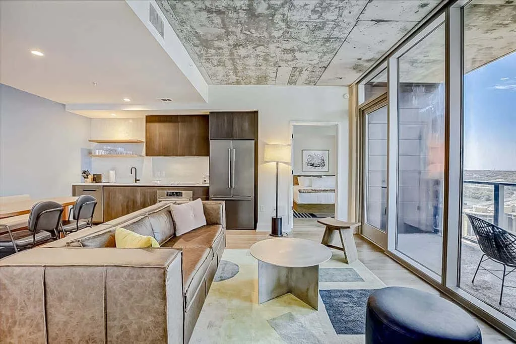An open-plan living room and kitchen with large windows overlooking the water.