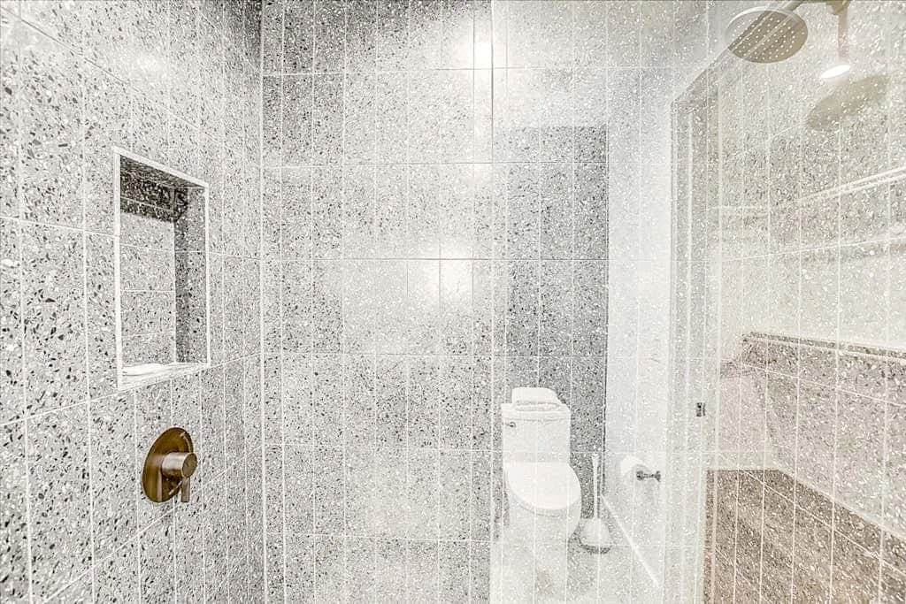 Un baño con azulejos, un inodoro y una mampara de ducha de vidrio.