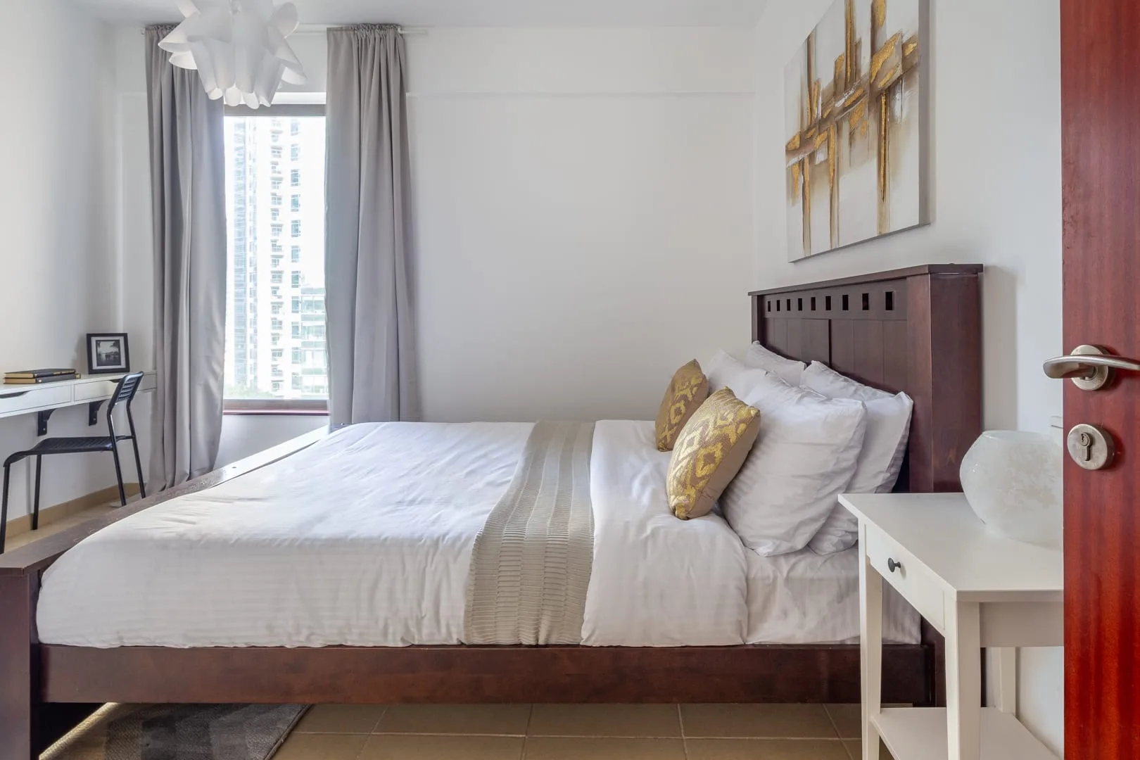 Un dormitorio luminoso con una cama arreglada y un escritorio junto a la ventana.