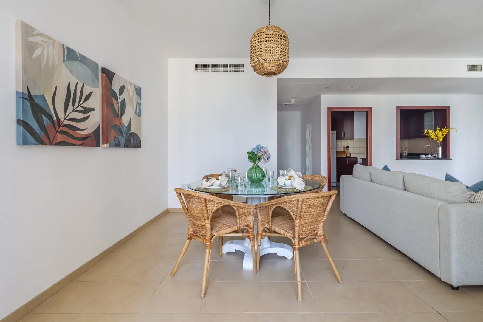 Un comedor con una mesa redonda de cristal y asientos tejidos junto a una sala de estar.