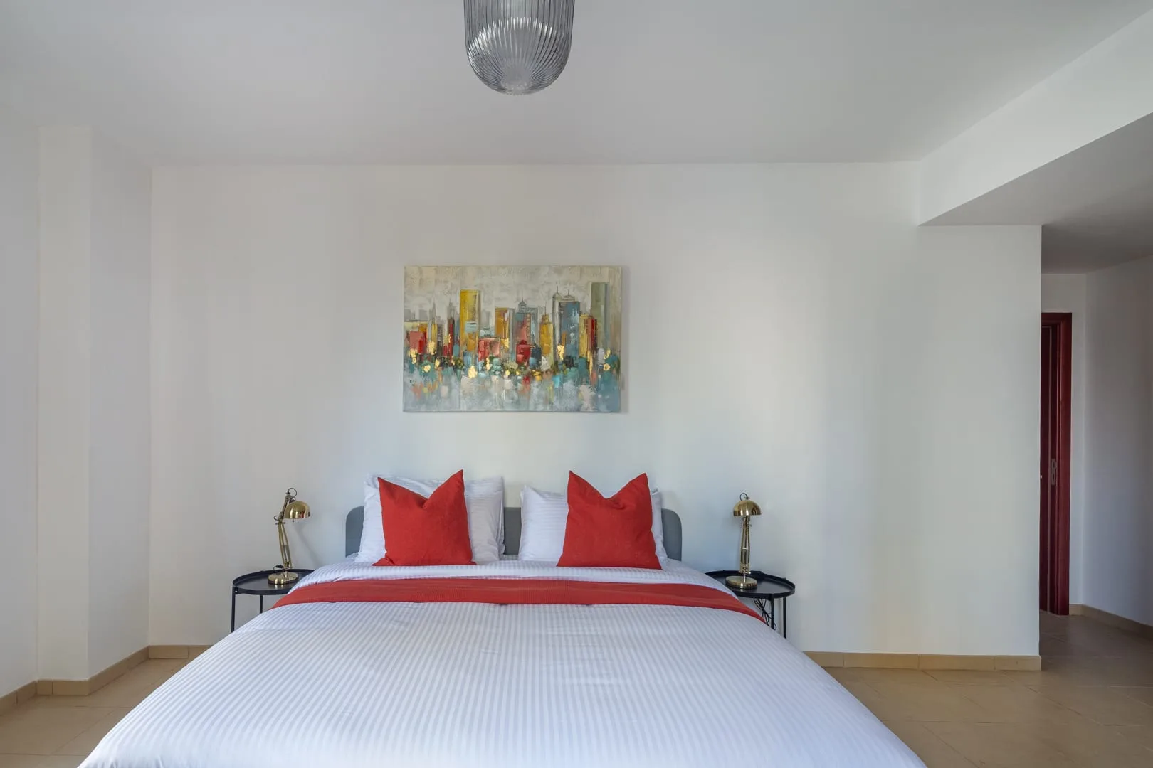 Un dormitorio con una cama vestida de blanco y rojo bajo una pintura colorida.