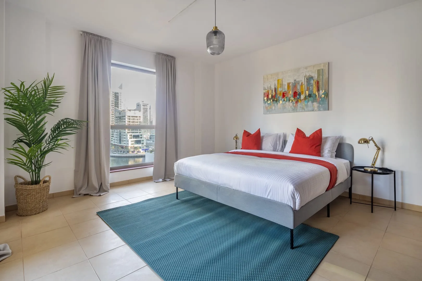 Un dormitorio luminoso con una cama, cojines de colores y una ventana grande.