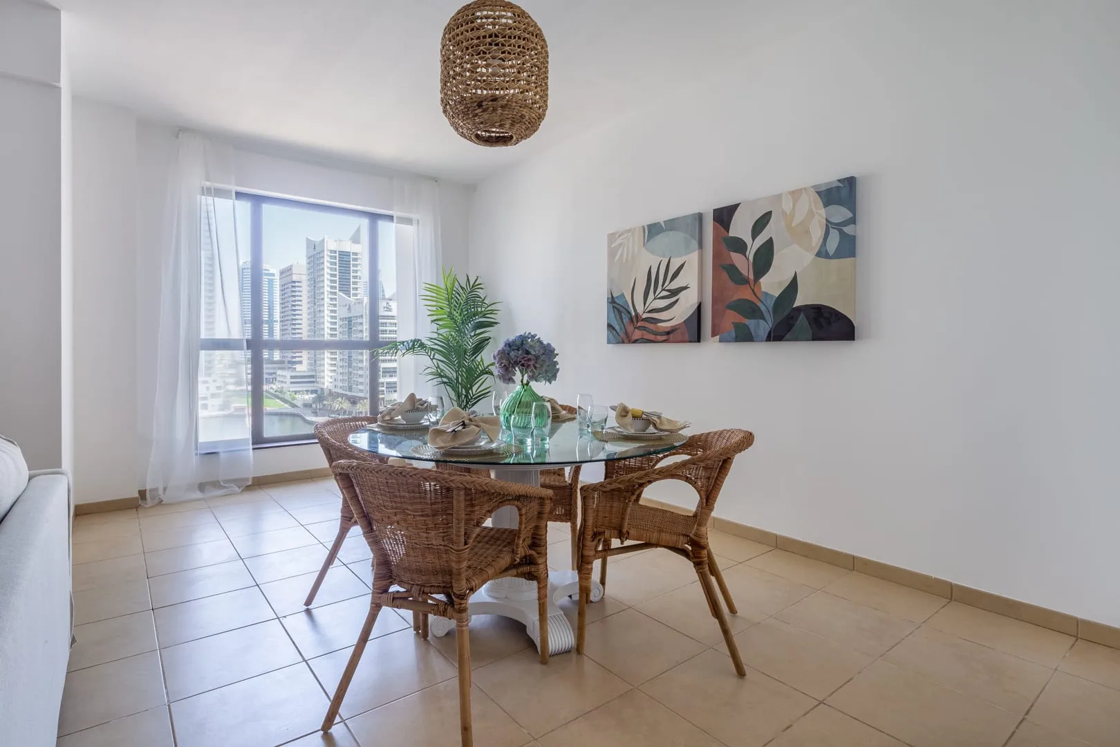 Comedor con una mesa de vidrio y asientos tejidos junto a una ventana grande.