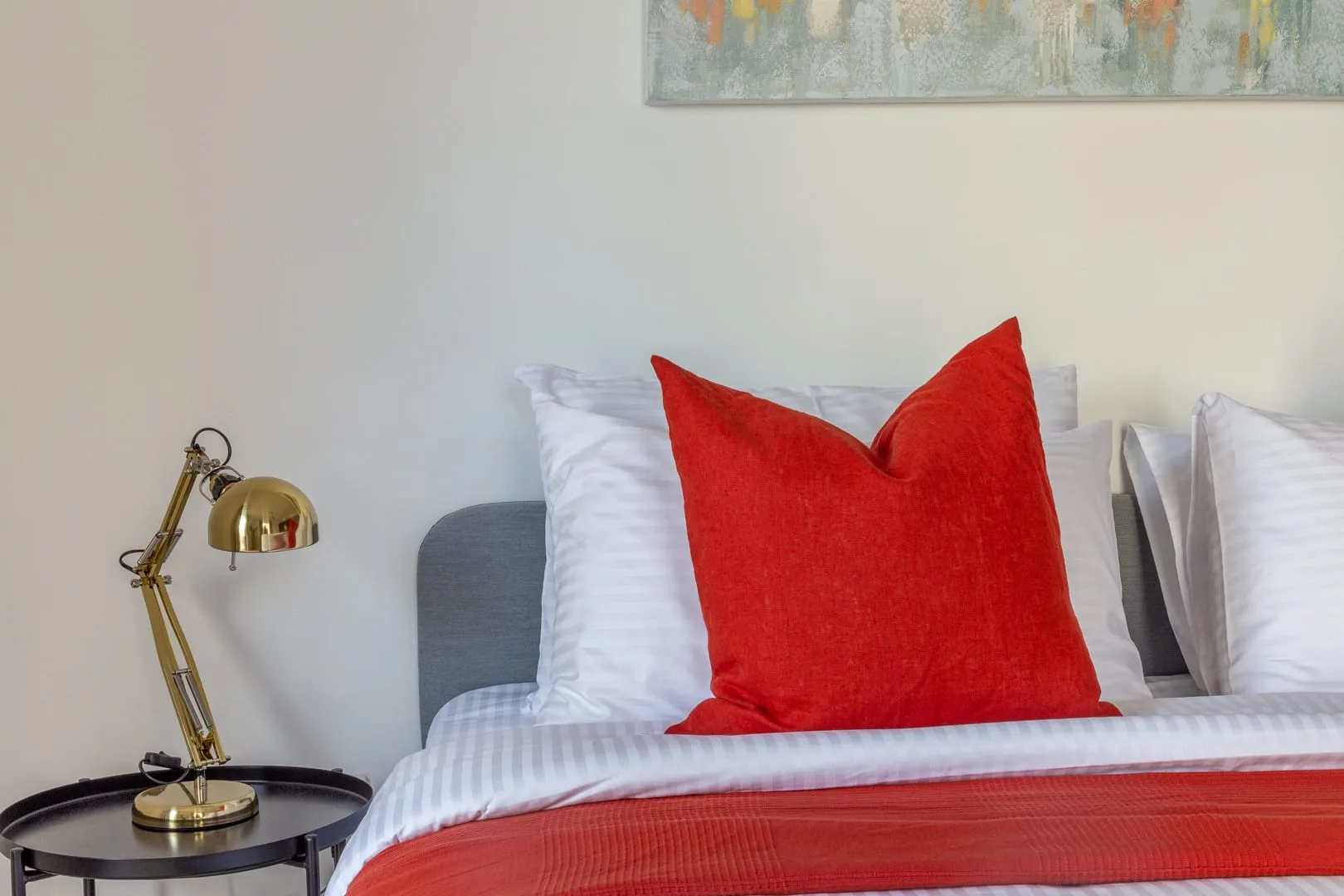 Una cama de dormitorio con almohadas blancas y un cojín decorativo rojo.