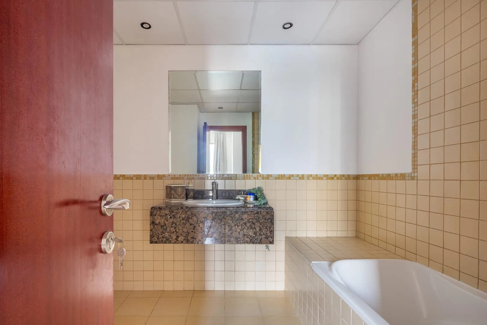 Un baño con azulejos, bañera, lavabo y un espejo grande en la pared.