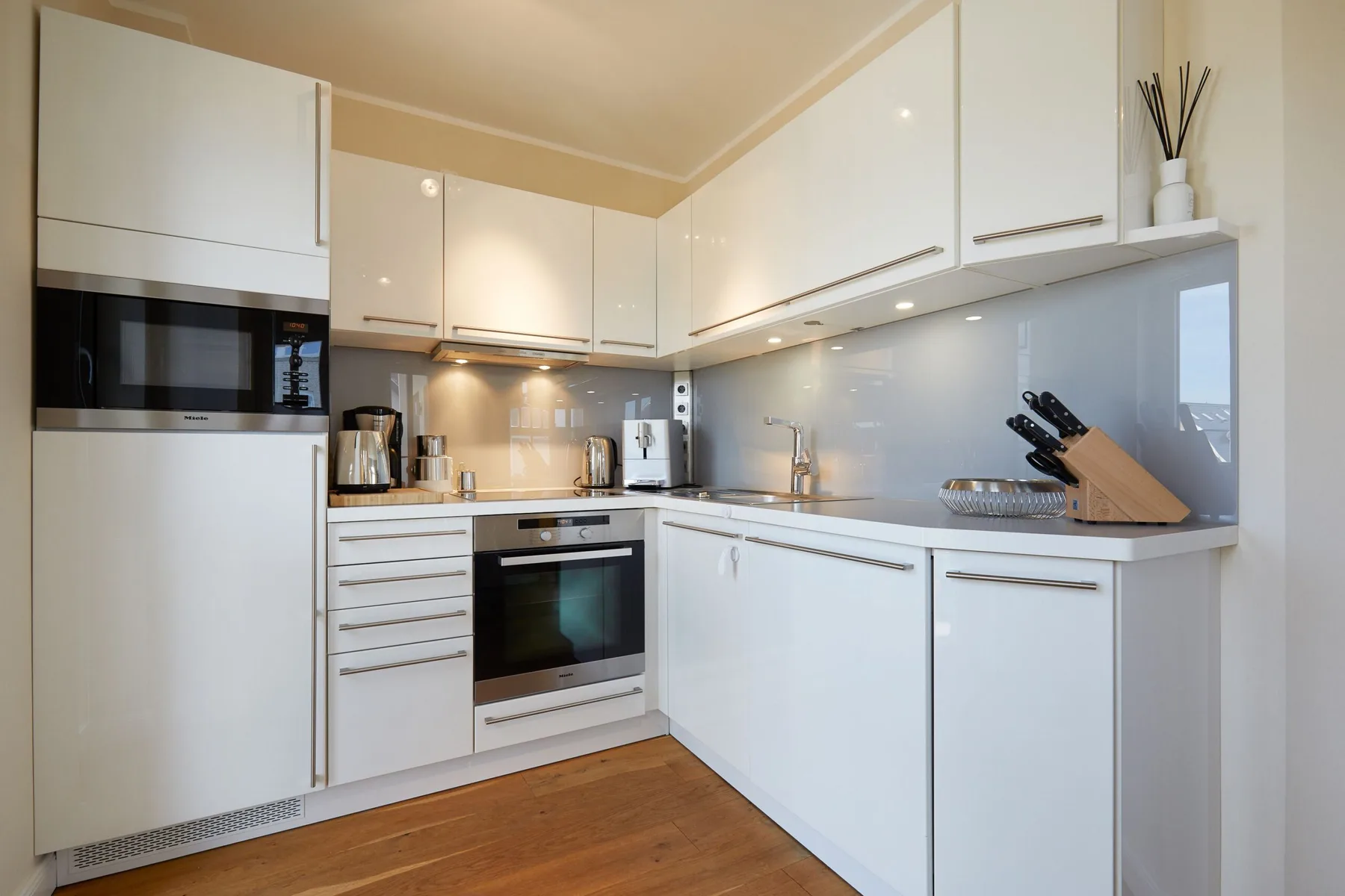 Una cocina moderna y luminosa con armarios blancos y suelo de madera.