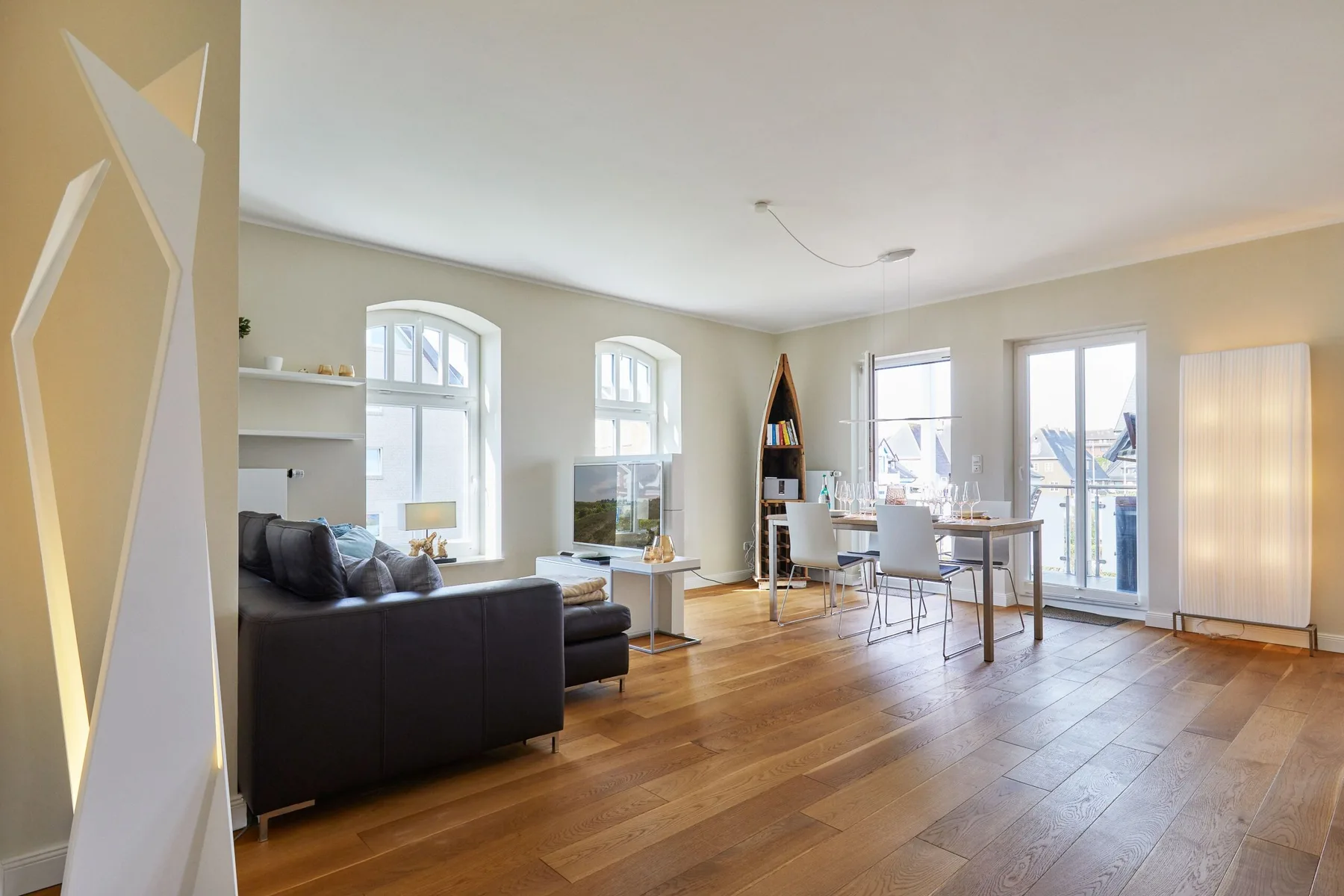 Una luminosa sala de estar y comedor con un sofá oscuro y una mesa junto a las ventanas.