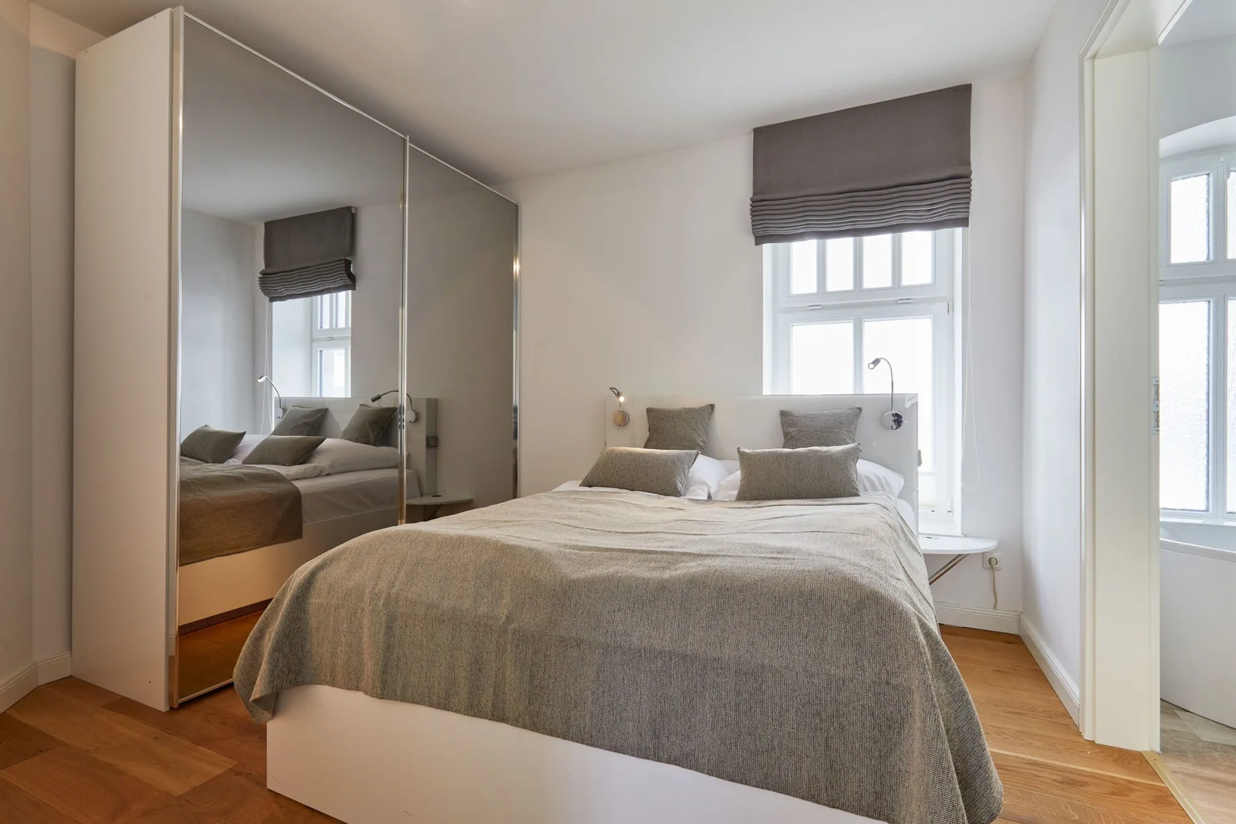 Un dormitorio con una cama bajo una ventana y armarios con espejo.