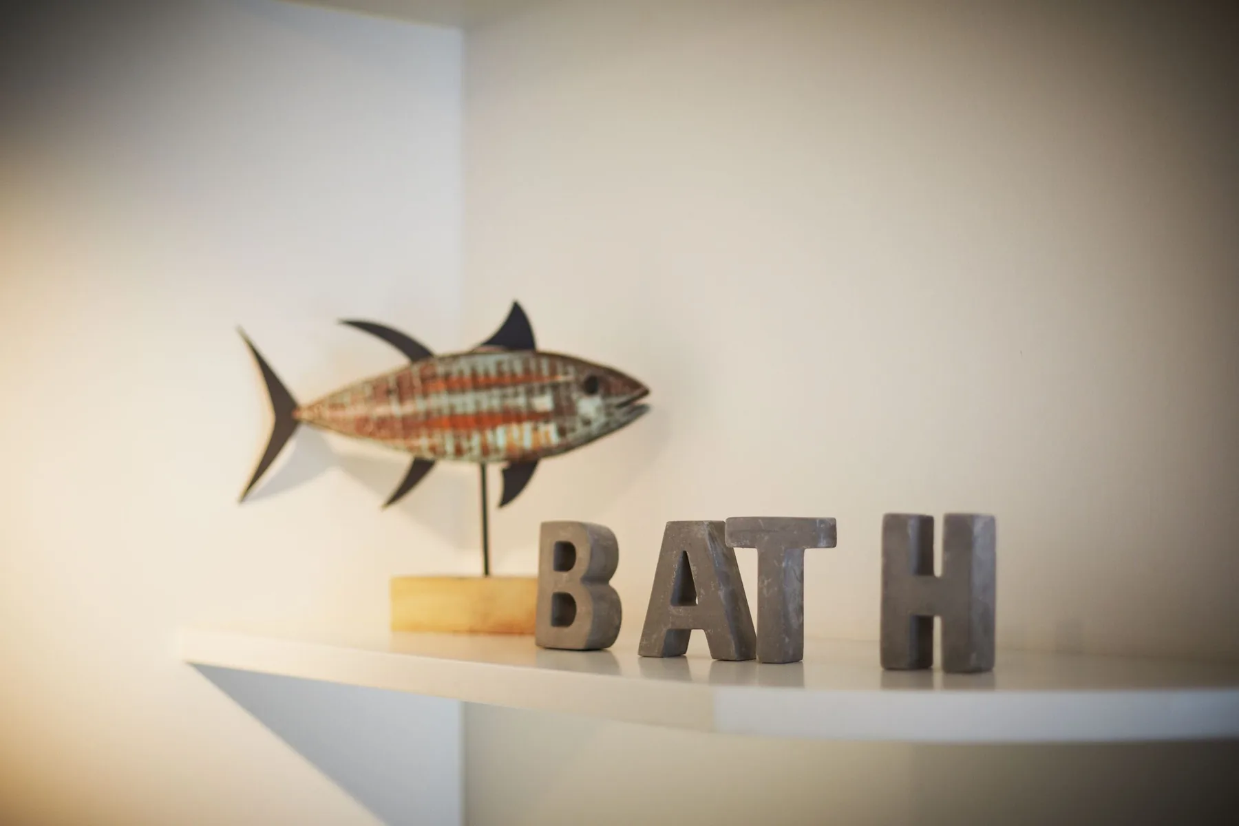 Un estante de pared muestra un pez decorativo y las letras que forman «BATH».