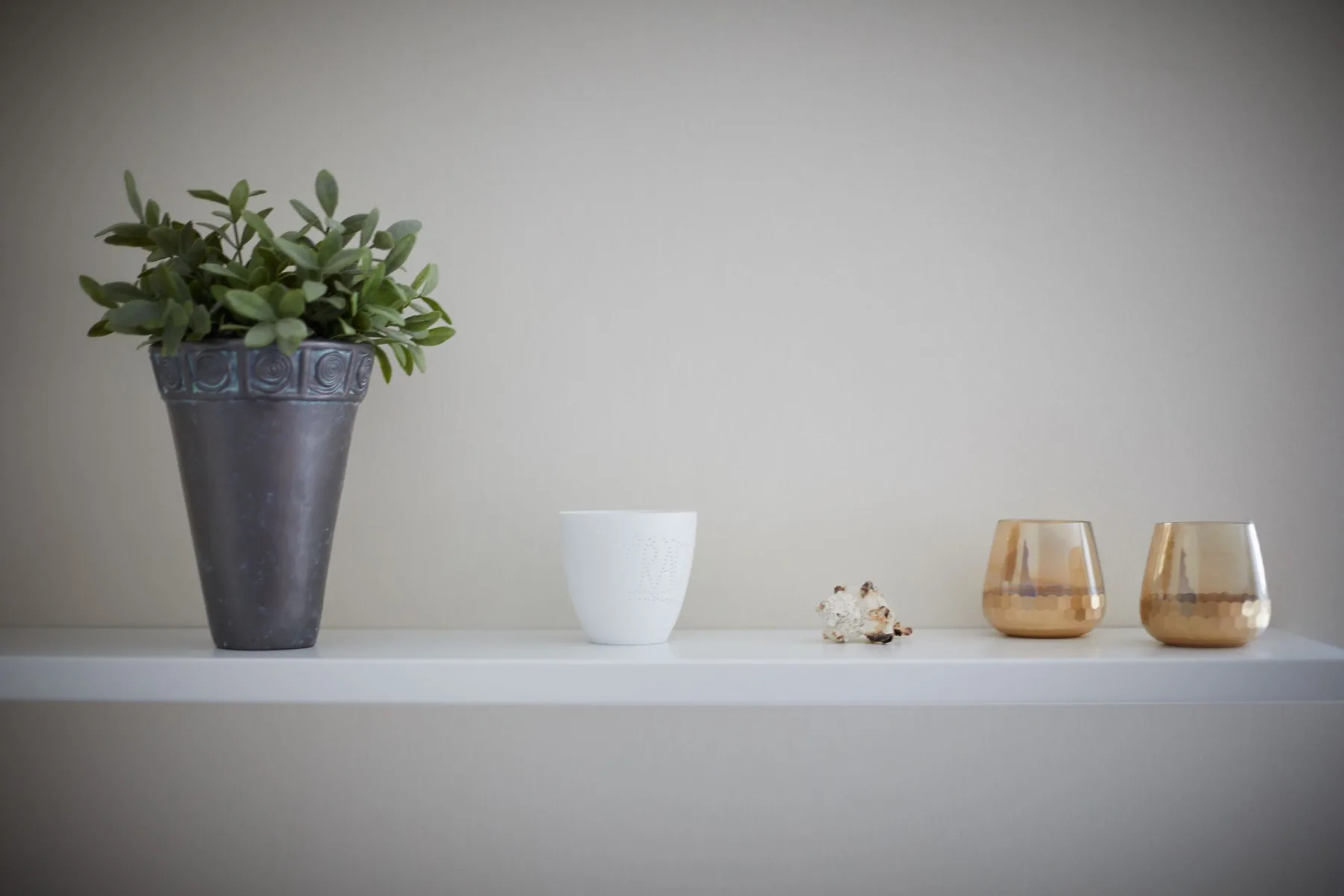 Una sencilla decoración sobre una repisa con una planta en maceta, una taza blanca y recipientes de vidrio ámbar.