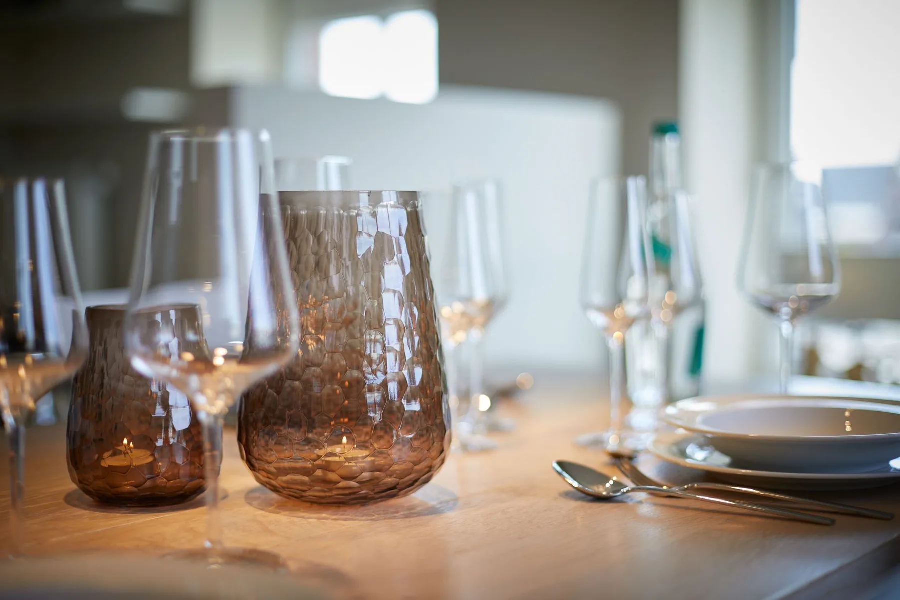 Una mesa de comedor está puesta con cristalería, platos y cubiertos.