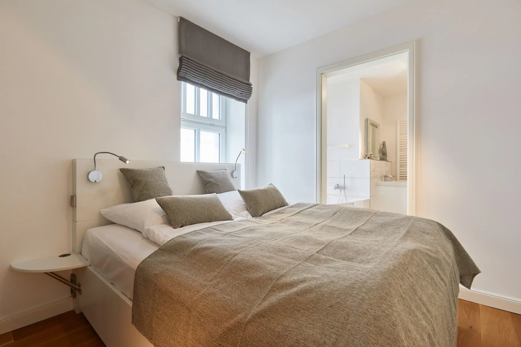 Un dormitorio con una cama bajo una ventana y una puerta abierta hacia un baño.
