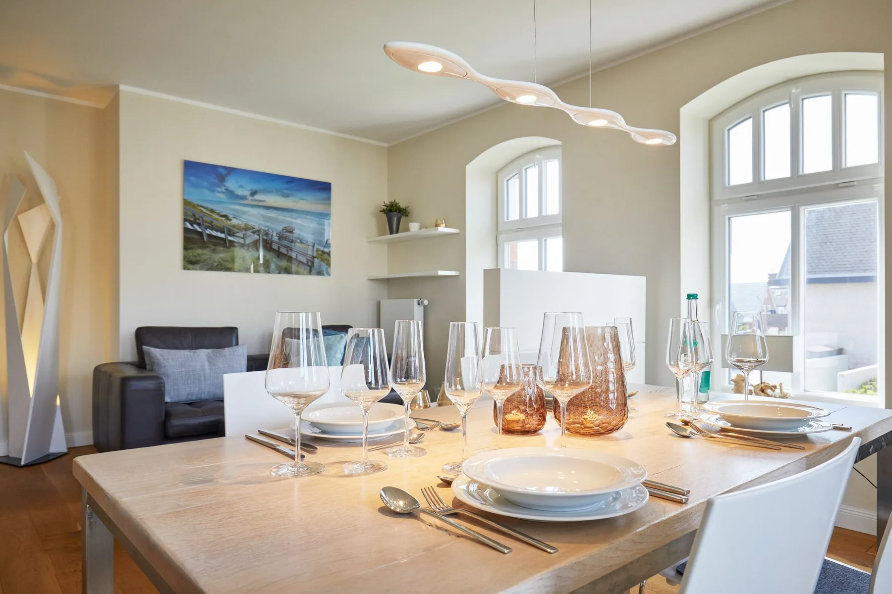 Una mesa de comedor con cristalería está junto a grandes ventanas arqueadas.