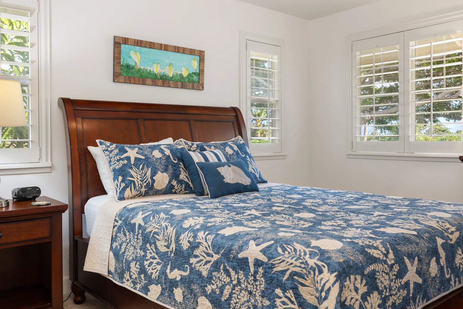 Un dormitorio con una cama cubierta con ropa de cama azul estampada junto a ventanas con contraventanas.