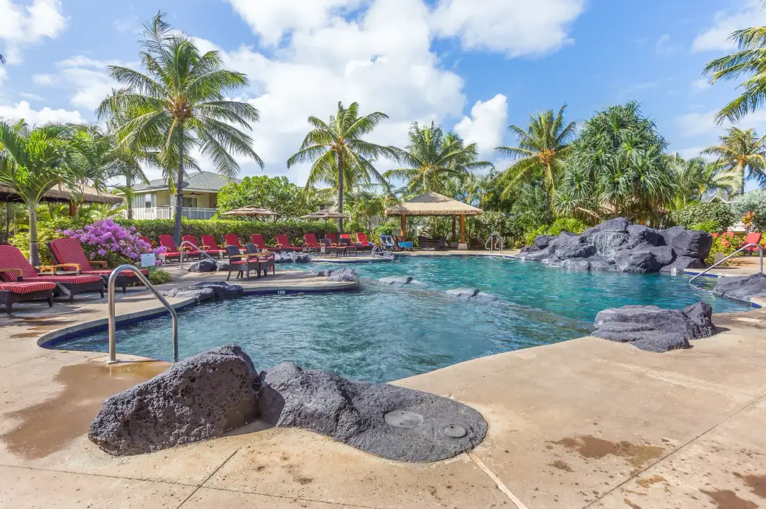 Una piscina tropical al aire libre está rodeada de palmeras y asientos para descansar.