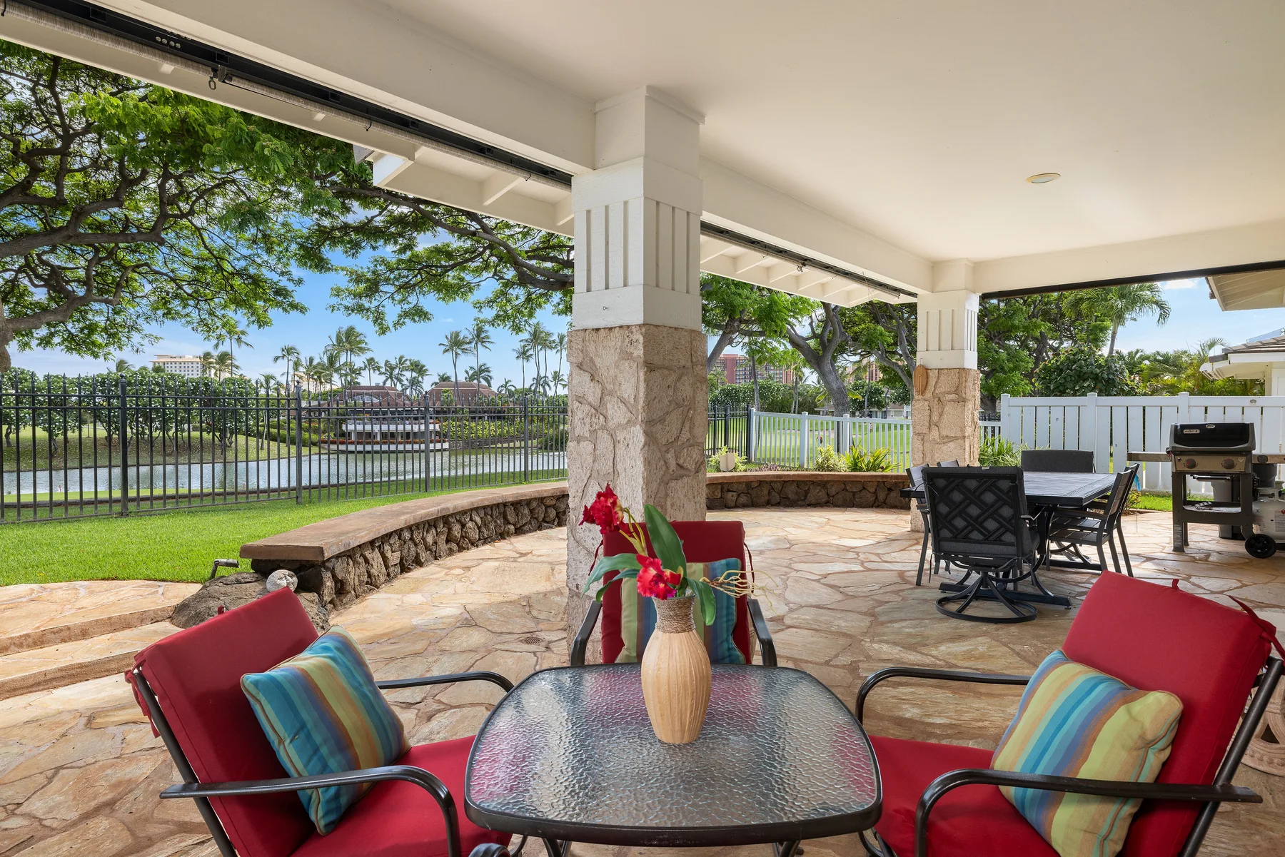 Un patio cubierto con asientos y una mesa da a un jardín verde.