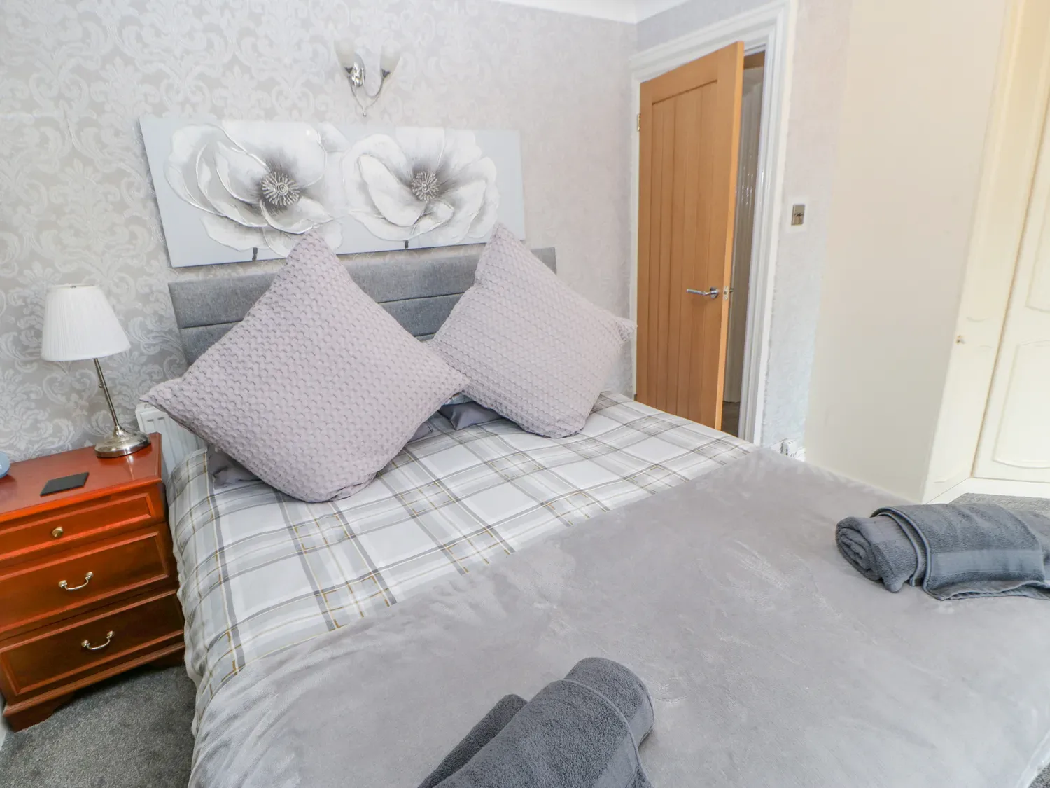 Un dormitorio con una cama cubierta con ropa de cama a cuadros grises y toallas dobladas al pie.