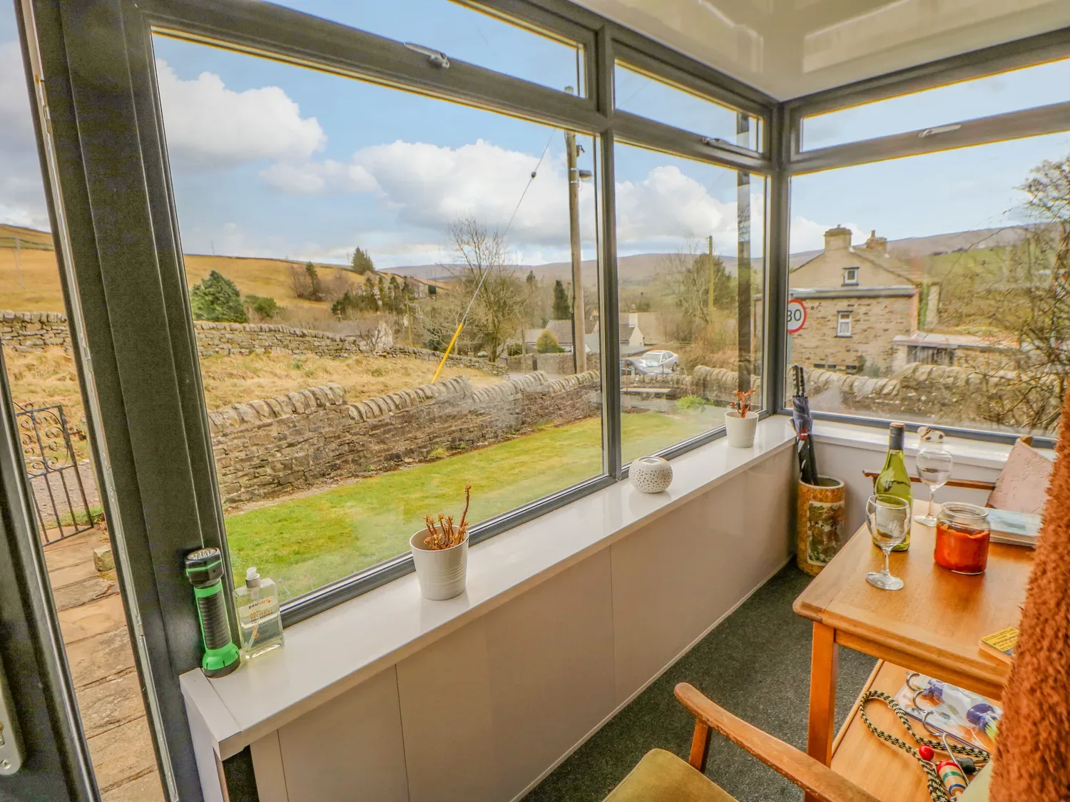Una sala acristalada con grandes ventanas con vistas a un muro de piedra y al campo, y una mesa con copas de vino y una botella en 1 Braeside, en Cowshill, cerca de Wearhead